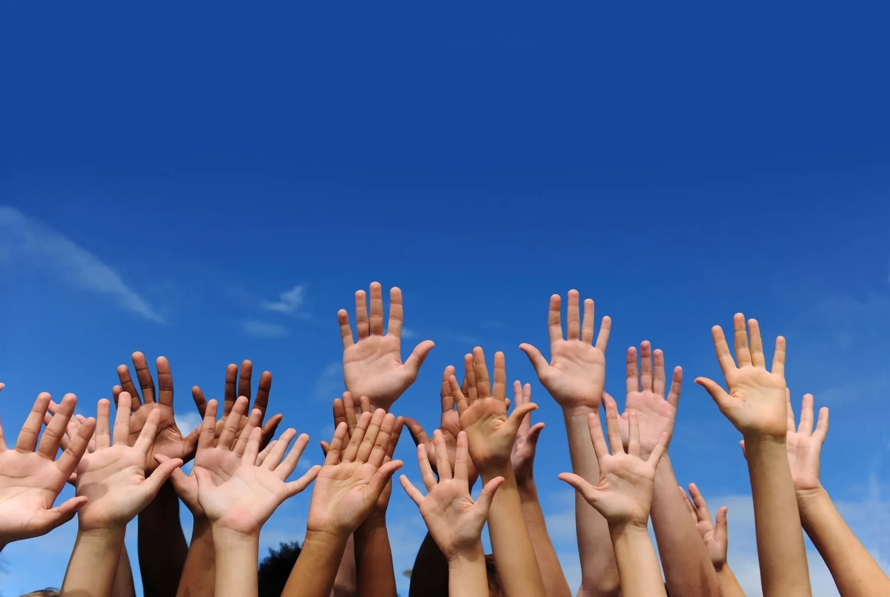 Hands raised in worship against a blue sky